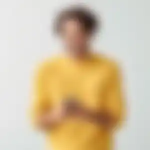 Ein lächelnder Mann in einem gelben Pullover schaut auf sein Handy, während er vor einem hellen Hintergrund steht.